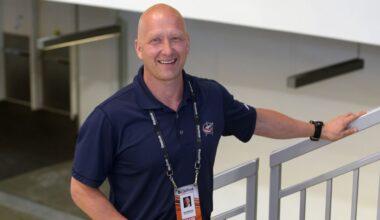jarmo kekalainen stands on stairway, wearing a columbus blue jackets polo, and smiles