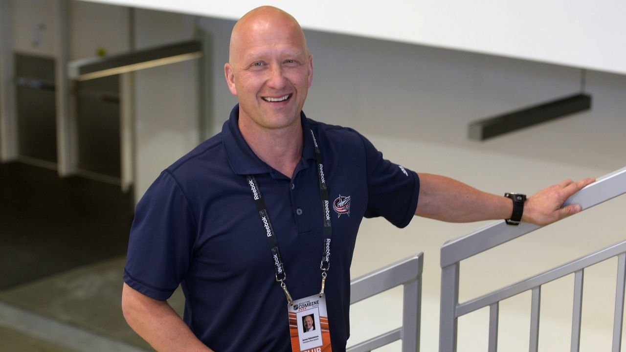 jarmo kekalainen stands on stairway, wearing a columbus blue jackets polo, and smiles