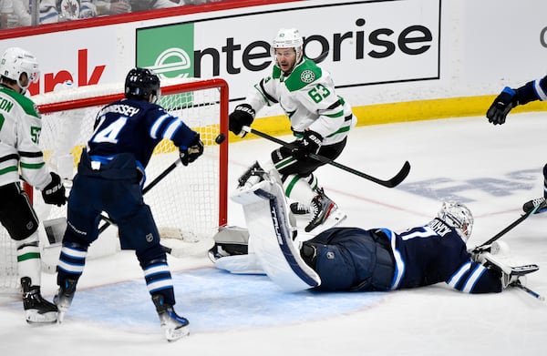 Winnipeg Jets goaltender Connor Hellebuyck, bottom right, gets a piece of the puck to deflect a shot by Dallas Stars' Evgenii Dadonov (63) during the second period of Game 2 of a second-round NHL hockey playoff series in Winnipeg, Manitoba, Friday, May 9, 2025. (Fred Greenslade/The Canadian Press via AP)