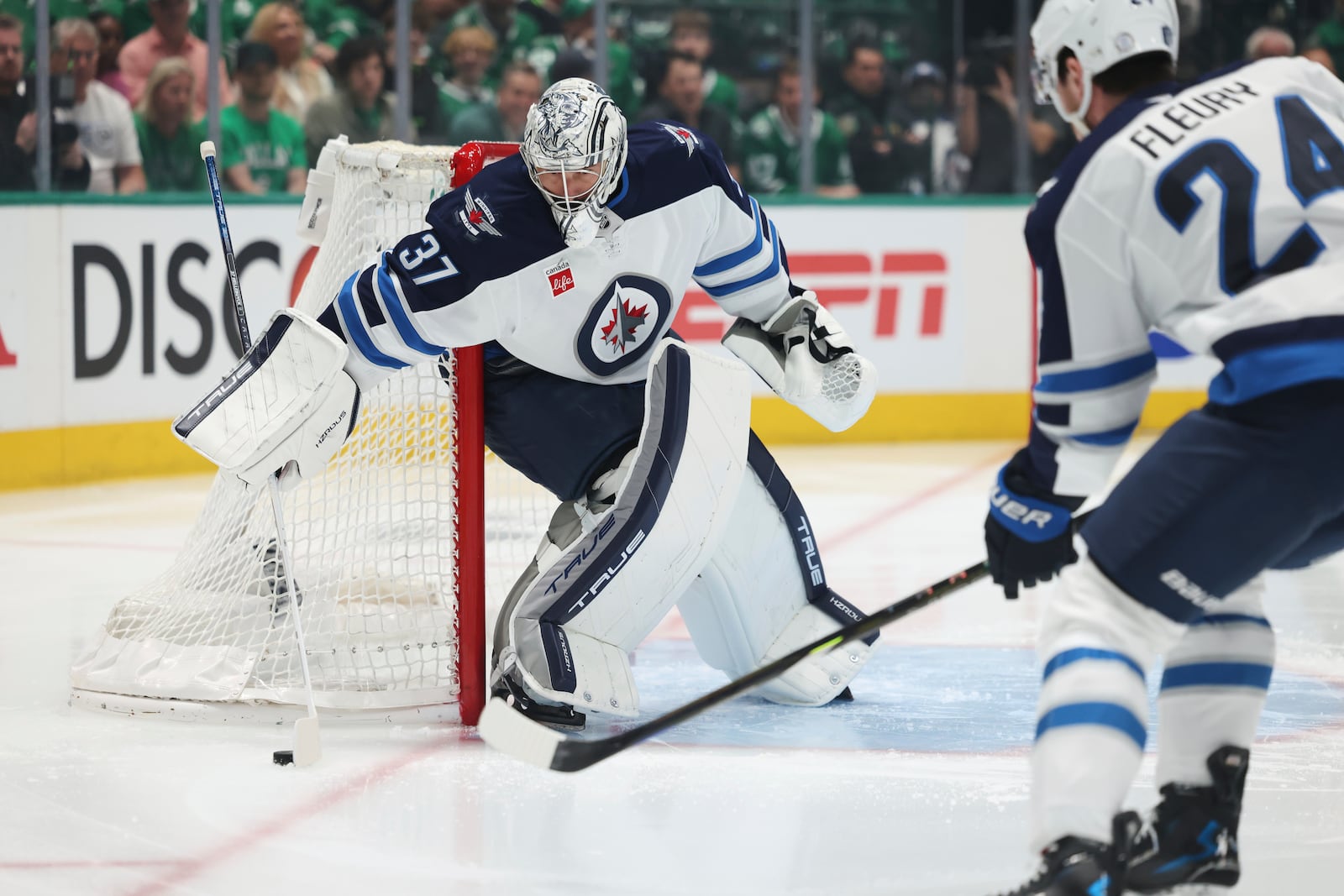Winnipeg Jets goaltender Connor Hellebuyck (37) cotrols the puck and as Haydn Fleury (24) moves in to take control in the first period of Game 4 of a second-round NHL hockey playoff series against the Dallas Stars in Dallas, Tuesday, May 13, 2025. (AP Photo/Gareth Patterson)