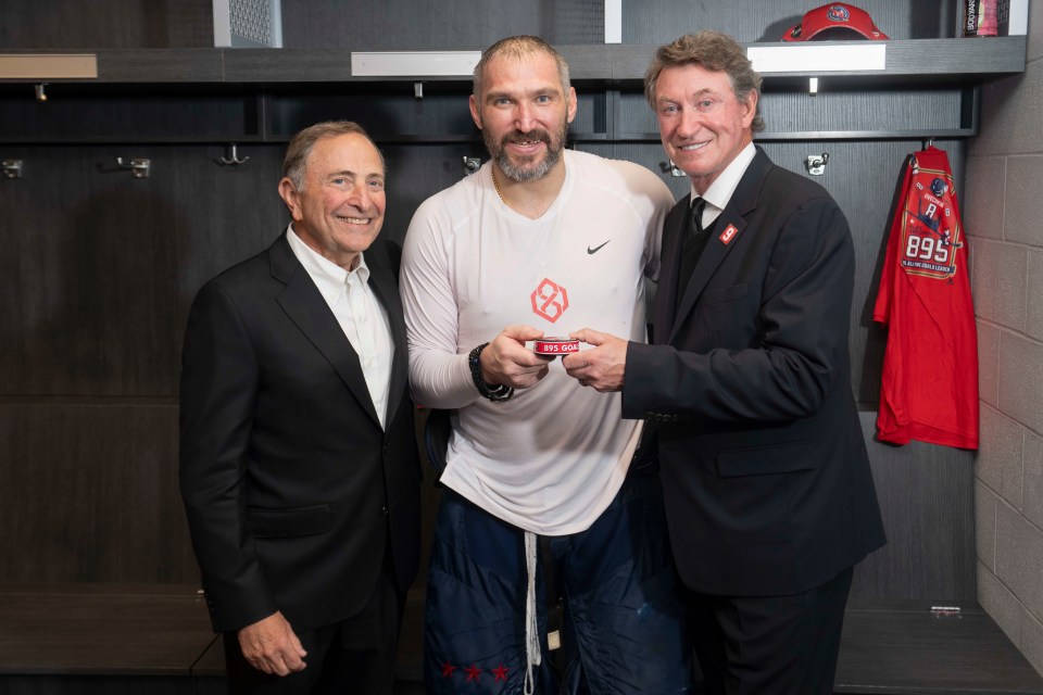 ELMONT, NEW YORK - APRIL 6: Alex Ovechkin #8 of the Washington Capitals poses for a photo with the puck from his 895th career goal with Wayne Gretzky and Gary Bettman in the locker room after a game against the New York Islanders at UBS Arena on April 6, 2025 in Elmont, New York. With this goal, Ovechkin passes Gretzky for the all-time goal scoring record. (Photo by Jess Rapfogel/NHLI via Getty Images)