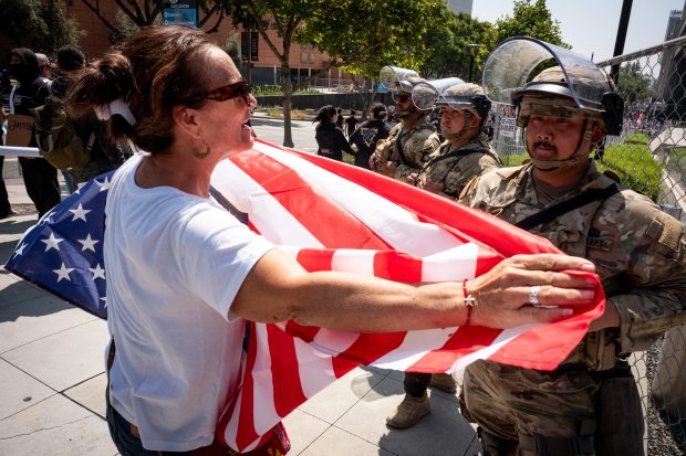 A No Kings protester faces a member of the National...