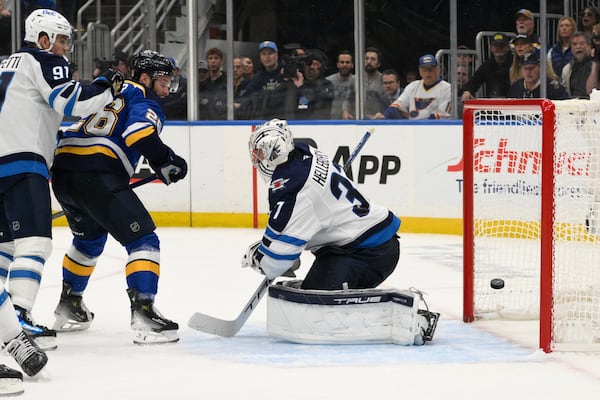 St. Louis Blues left wing Nathan Walker (26) and Winnipeg Jets center Cole Perfetti (91) look on as Jets goaltender Connor Hellebuyck gives up a goal during the second period in Game 6 of an NHL hockey first-round playoff series Friday, May 2, 2025, in St. Louis. (AP Photo/Jeff Le)