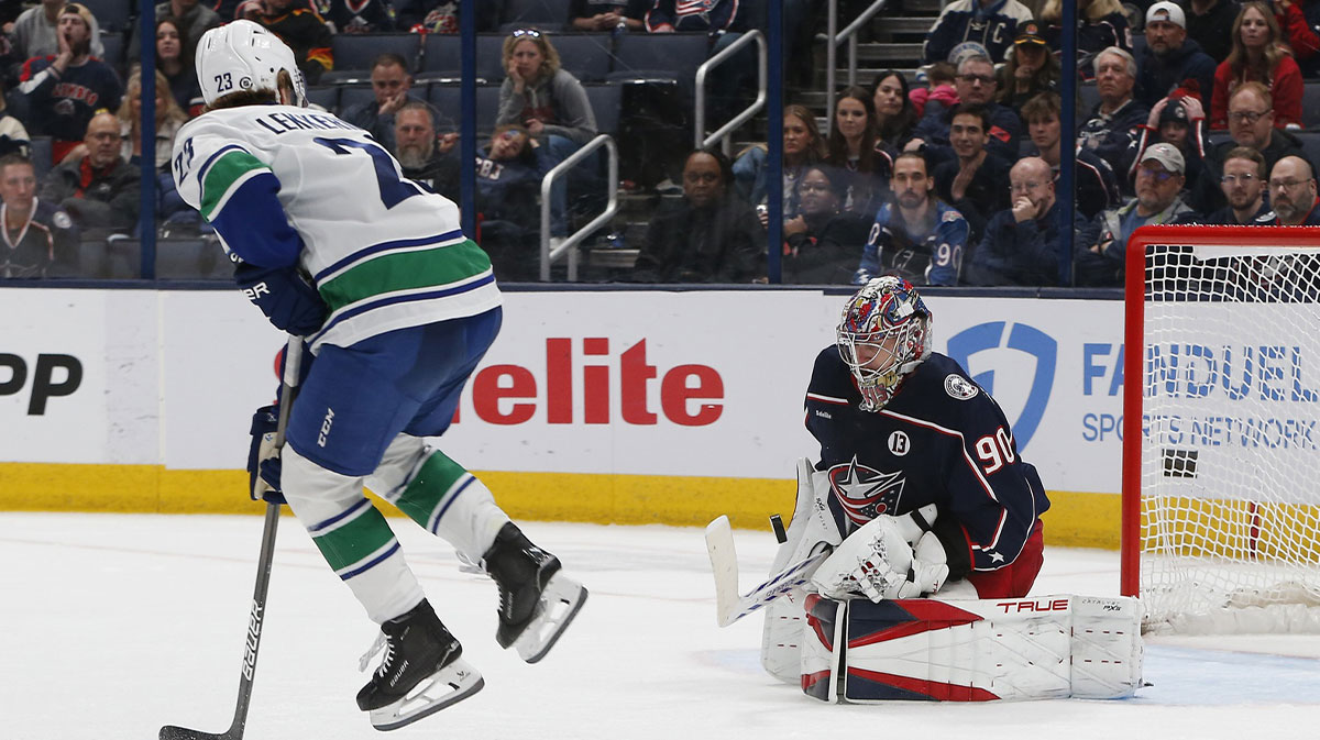 Vancouver Canucks right wing Jonathan Lekkerimaki (23) jumps to avoid the shot attempt as Columbus Blue Jackets goalie Elvis Merzlikins (90) makes a save during overtime at Nationwide Arena.