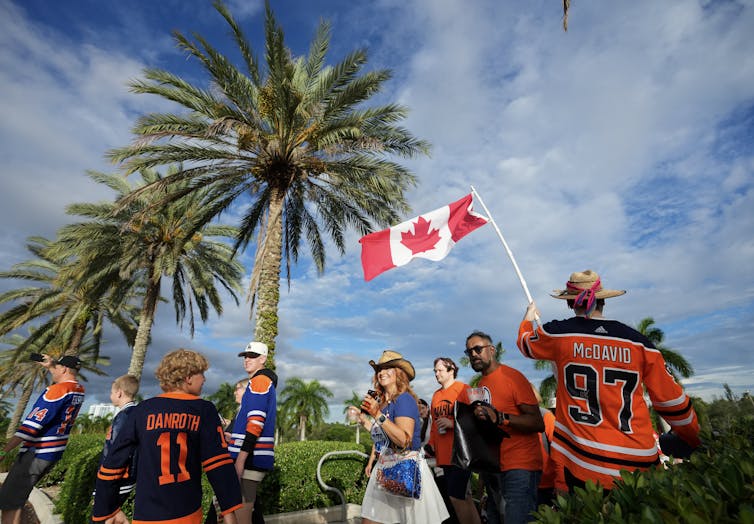 A person in a McDavid hockey jersey waves a Canadian flag while other people in hockey jerseys walk past them