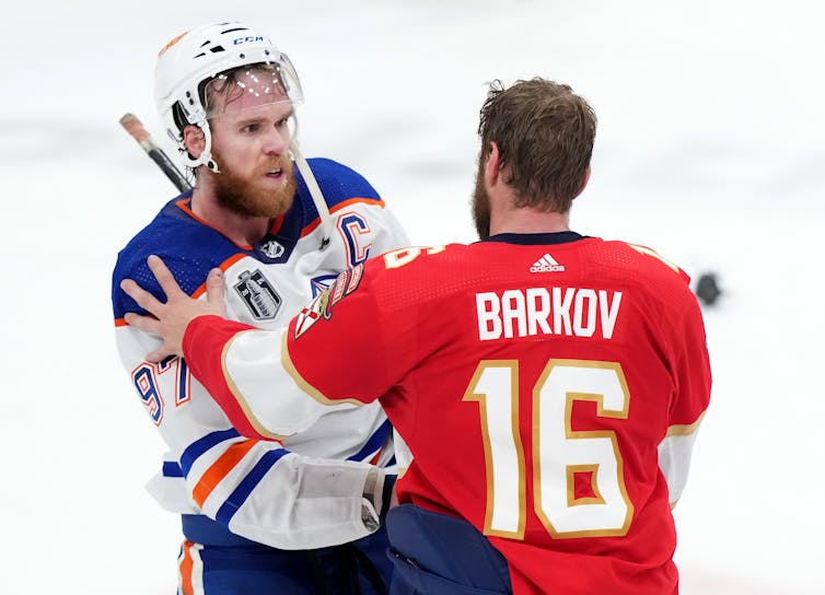 McDavid, with his helmet unbuckled, shakes Barkov's hand while Barkove places his left hand on McDavid's shoulder.