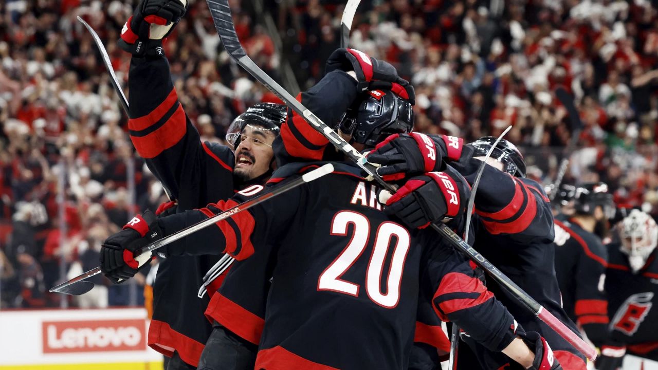 Carolina Hurricanes' Seth Jarvis, left, salutes the crowd from the celebration of Sebastian Aho's game-winning goal during the second overtime period of Game 5 of an NHL hockey Stanley Cup first-round playoff series against the New Jersey Devils in Raleigh, N.C., Tuesday, April 29, 2025. (AP Photo/Karl DeBlaker)