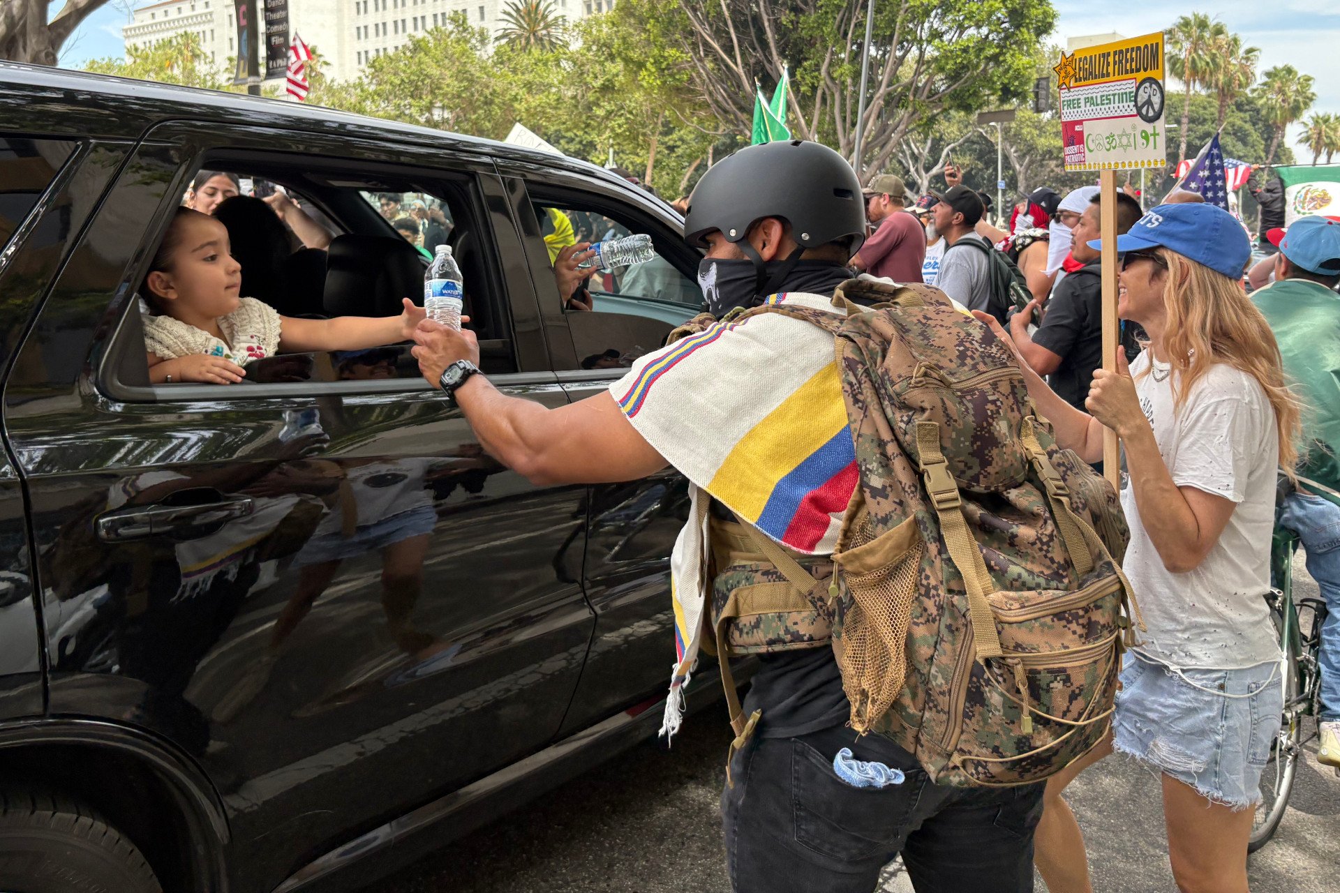 A young girl hands a protester a bottle of water at the No Kings protest in Los Angeles, California, on June 14, 2025.