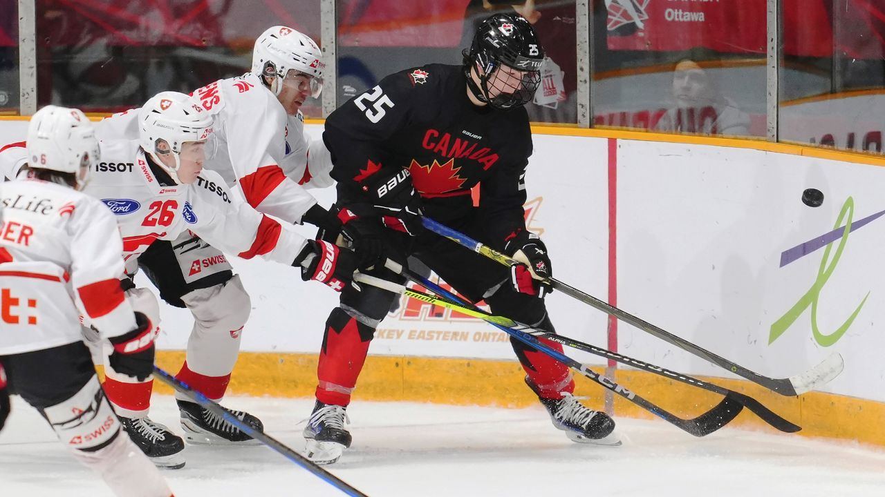 hockey defenseman in black jersey fights two players in white jerseys for control of the puck in a corner of the ice