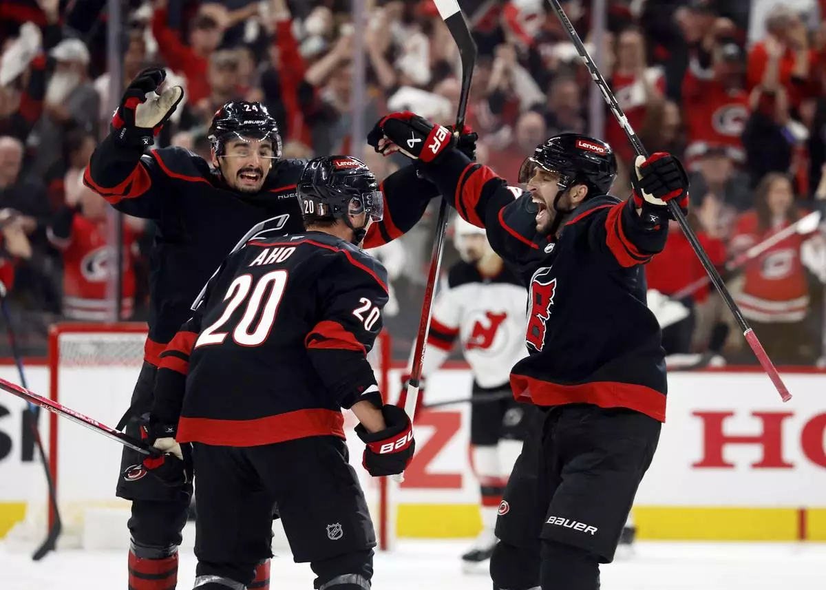 Carolina Hurricanes' Seth Jarvis, left, and Shayne Gostisbehere, right, congratulate Sebastian Aho (20) on his game-winning overtime goal during the second overtime period of Game 5 of an NHL hockey Stanley Cup first-round playoff series against the New Jersey Devils in Raleigh, N.C., Tuesday, April 29, 2025. (AP Photo/Karl DeBlaker)