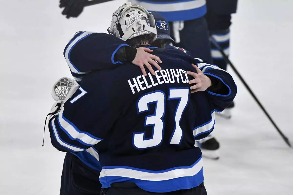Winnipeg Jets goaltender Eric Comrie, left, hugs goaltender Connor Hellebuyck (37) after the Jets defeated the St. Louis Blues in Game 7 in an NHL hockey first-round playoff series in Winnipeg, Manitoba, Sunday, May 4, 2025. (Fred Greenslade/The Canadian Press via AP)