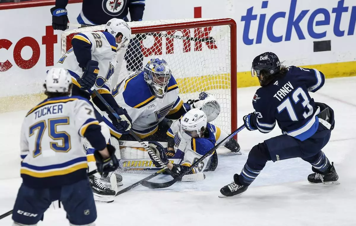 St. Louis Blues' Jake Neighbours (63) crashes into Blues goaltender Joel Hofer (30) as he saves a shot by Winnipeg Jets' Brandon Tanev (73) during third-period NHL hockey game action in Winnipeg, Manitoba, Monday, April 7, 2025. (John Woods/The Canadian Press via AP)