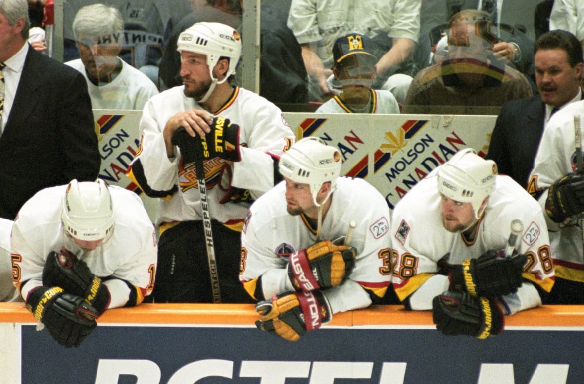 Hockey players hang their heads while watching from the sidelines of an arena ice rink.