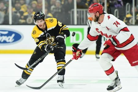 Apr 5, 2025; Boston, Massachusetts, USA; Boston Bruins center Vinni Lettieri (95) shoots the puck past Carolina Hurricanes defenseman Jaccob Slavin (74) during the first period at TD Garden. Mandatory Credit: Bob DeChiara-Imagn Images
