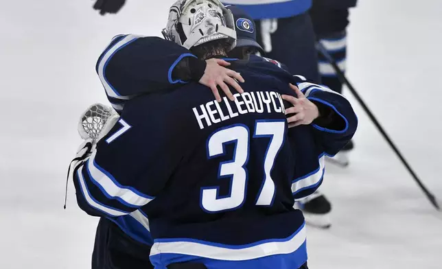 Winnipeg Jets goaltender Eric Comrie, left, hugs goaltender Connor Hellebuyck (37) after the Jets defeated the St. Louis Blues in Game 7 in an NHL hockey first-round playoff series in Winnipeg, Manitoba, Sunday, May 4, 2025. (Fred Greenslade/The Canadian Press via AP)