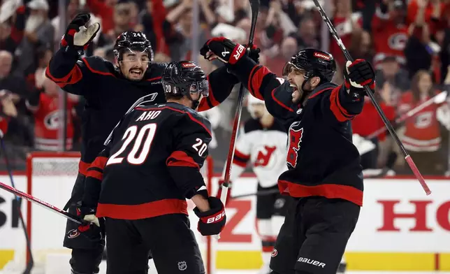 Carolina Hurricanes' Seth Jarvis, left, and Shayne Gostisbehere, right, congratulate Sebastian Aho (20) on his game-winning overtime goal during the second overtime period of Game 5 of an NHL hockey Stanley Cup first-round playoff series against the New Jersey Devils in Raleigh, N.C., Tuesday, April 29, 2025. (AP Photo/Karl DeBlaker)
