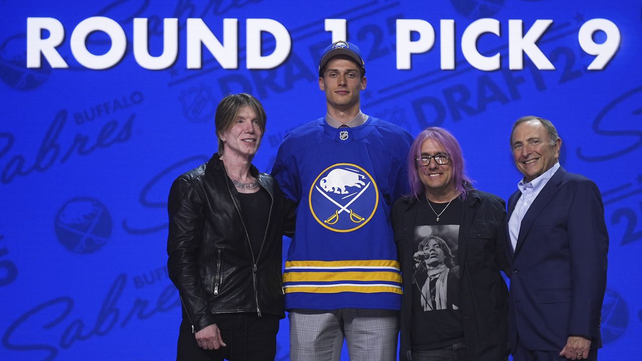Radim Mrtka, middle left, stands between The Goo Goo Dolls' John Rzeznik, left, and Robby Takac, middle right, and NHL commissioner Gary Bettman after being drafted by the Buffalo Sabres during the NHL hockey draft Friday, June 27, 2025, in Los Angeles. (AP Photo/Damian Dovarganes)