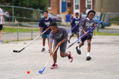 children play street hockey outside in a fenced area