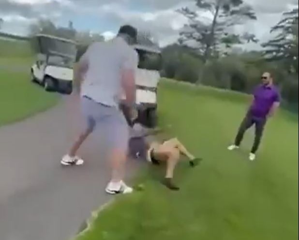 A fight breaks out on a golf course; a man is thrown to the ground.