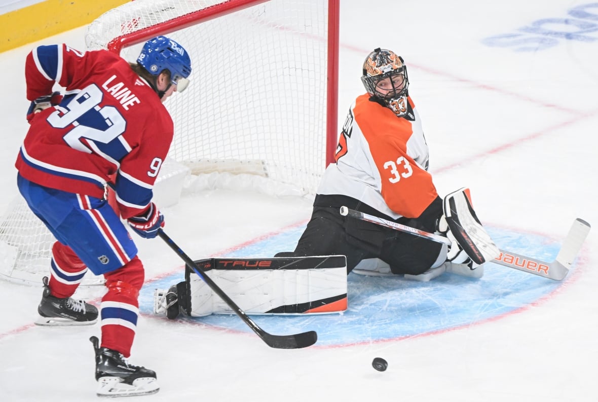 A hockey player stands in front of a goaltender as a puck is loose in front of the net