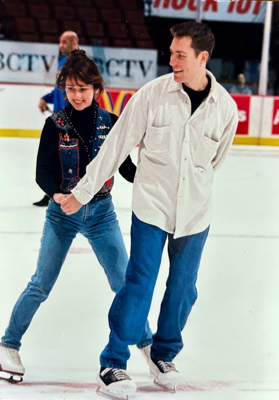 A man and a woman hold hands while skating on an ice rink.
