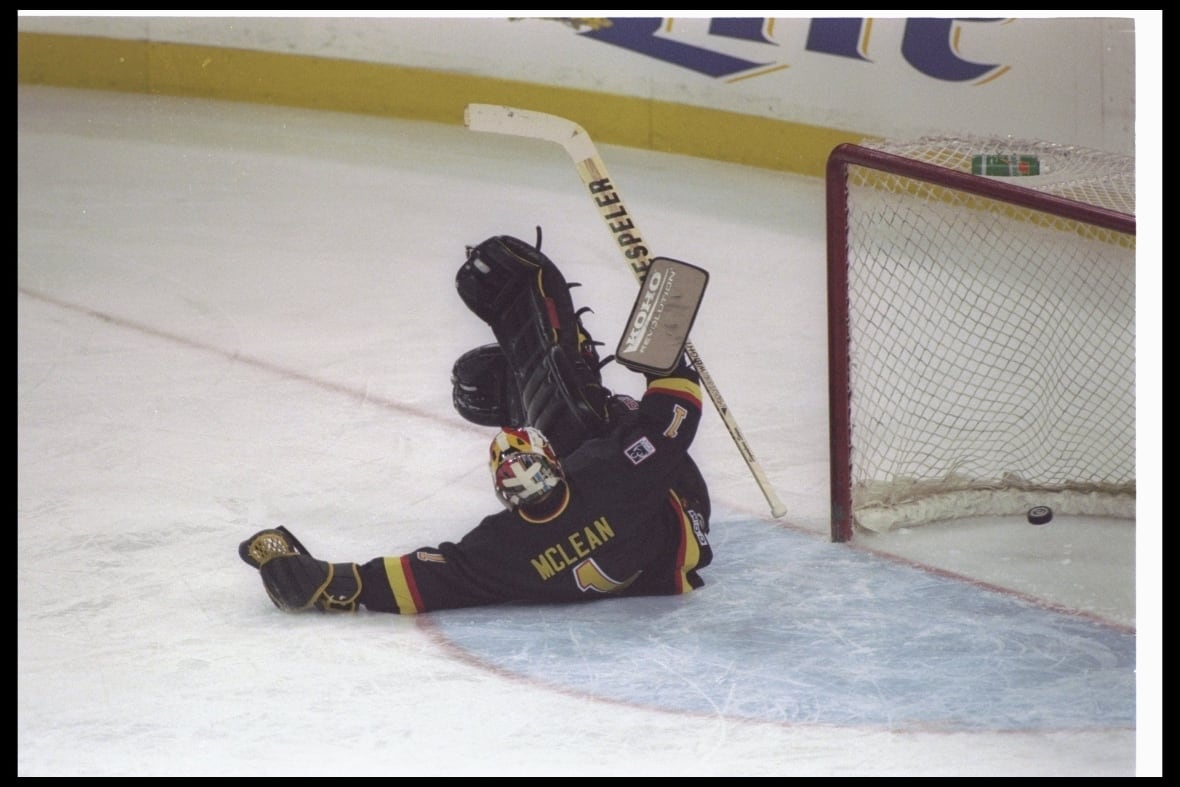 A hockey goalie trips and falls on the ice nearby his net.