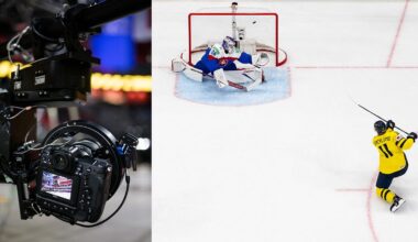 Close-up of a professional camera capturing a hockey game; next to it, a hockey player in yellow shoots the puck towards the goal as the opposing goalie makes a save attempt on the ice.