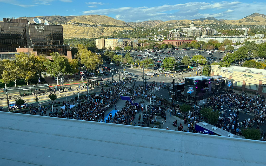 Large crowd at an outdoor event with hills and urban buildings in the background.
