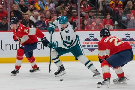 Dec 7, 2024; Sunrise, Florida, USA; San Jose Sharks center Klim Kostin (10) moves the puck between Florida Panthers defenseman Niko Mikkola (77) and right wing Mackie Samoskevich (25) during the second period at Amerant Bank Arena. Mandatory Credit: Sam Navarro-Imagn Images