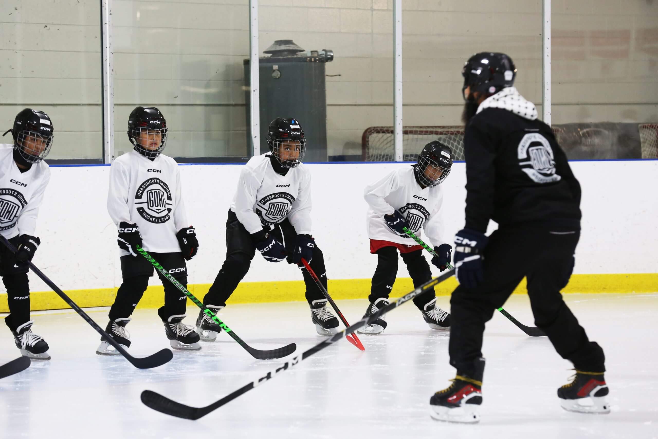A group of fifth-grade students in white hockey jerseys and black helmets face a coach at a Hockey Diversity Alliance-sponsored practice in 2024.