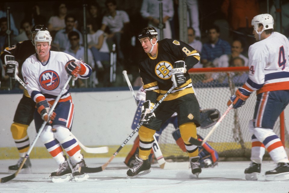 Canadian ice hockey player Cam Neely (#8 in black) of the Boston Bruins waits in front of the net for the puck while Gord Dineen (#2 at left) of the New York Islanders and an unidentified teammate (#4 at right) look to stop him during a game at the Nassau Coliseum, Uniondale, New York, October 1986. (Photo by Bruce Bennett Studios via Getty Images Studios/Getty Images)