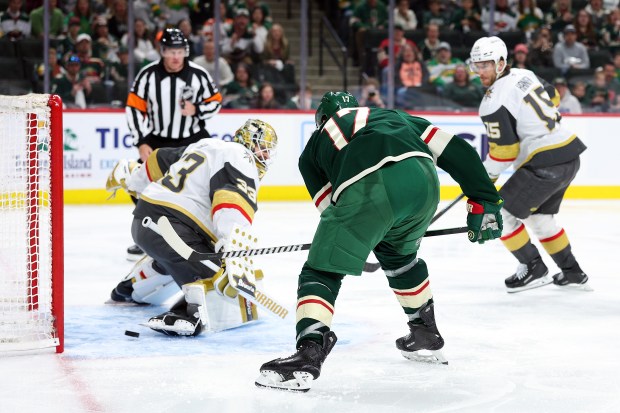 Hockey players skate towards a goal post.