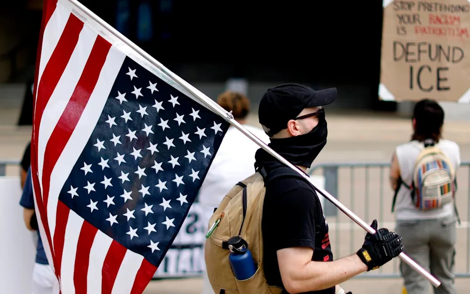 A masked protester carries an American flag hung upside down.
