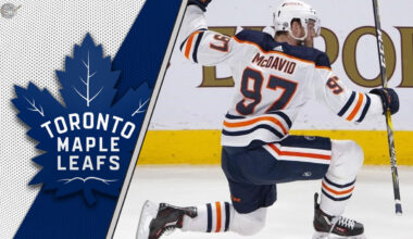 Connor McDavid celebrates a goal during a game, with the Toronto Maple Leafs logo in the background, fueling NHL rumors of a potential trade.