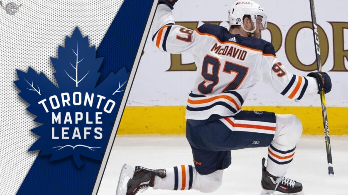 Connor McDavid celebrates a goal during a game, with the Toronto Maple Leafs logo in the background, fueling NHL rumors of a potential trade.