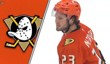 Anaheim Ducks center Mason McTavish skates with the puck during an NHL game, with Anaheim Ducks logo in the background