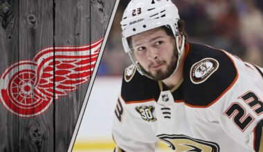 An image of Mason McTavish in his Anaheim Ducks jersey, looking focused during a game, with the Detroit Red Wings logo in the background.