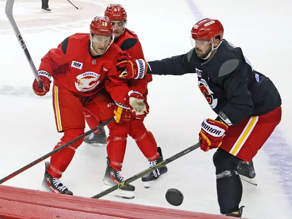  Calgary Flames forwards from left; Jonathan Huberdeau, Matt Coronato and defenceman MacKenzie Weegar jostle for the puck along the boards.