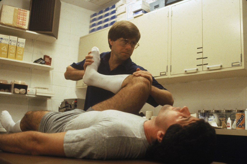 Islanders trainer Ron Waske stretches defenseman Gordie Lane's hamstring in 1983.