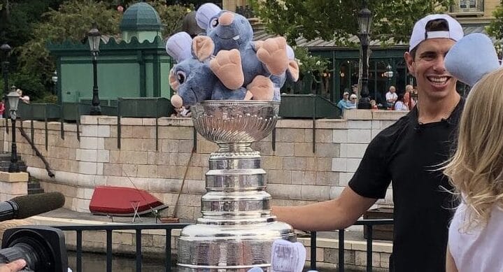 A man and children stand by a Stanley Cup filled with Remy plushies from Ratatouille at an EPCOT outdoor event.
