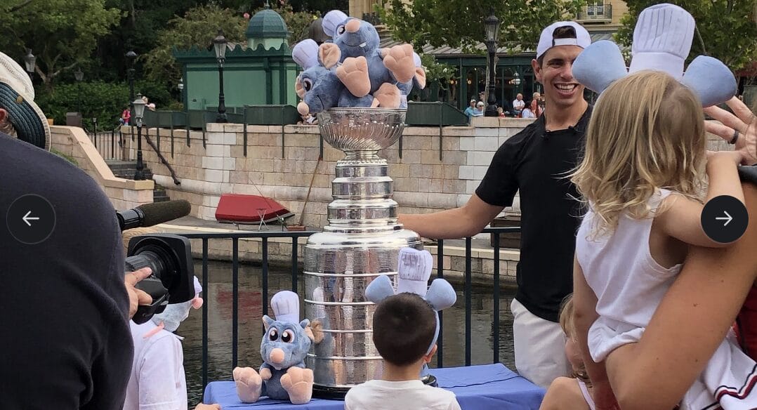 A man and children stand by a Stanley Cup filled with Remy plushies from Ratatouille at an EPCOT outdoor event.