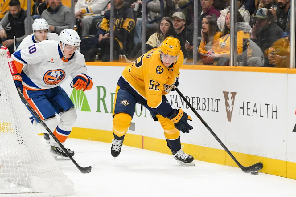 Apr 8, 2025; Nashville, Tennessee, USA; Nashville Predators right wing Matthew Wood (52) and New York Islanders right wing Simon Holmstrom (10) battle for the puck during the first period at Bridgestone Arena. Mandatory Credit: Steve Roberts-Imagn Images
