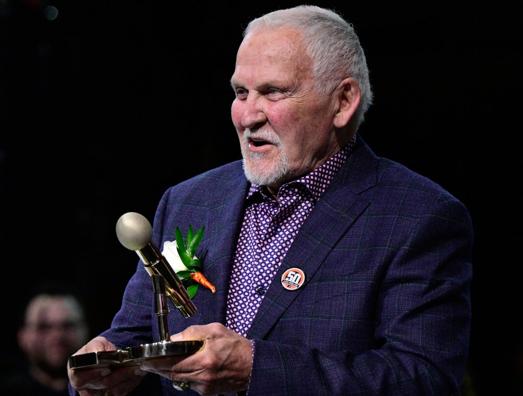 Bernie Parent, former Philadelphia Flyers goalie, holds a microphone and trophy while speaking during a ceremony for Lou Nolan.