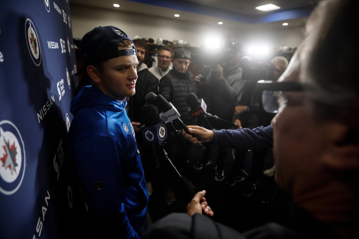 A man with a blue hoodie and backwards baseball cap speaks with reporters during a media scrum.
