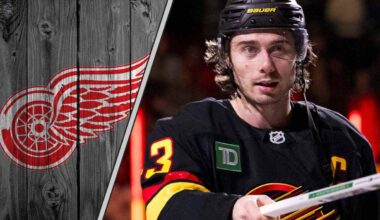 Quinn Hughes skates in his Vancouver Canucks jersey, looking focused during an NHL game, with the Detroit Red Wings logo in the background.