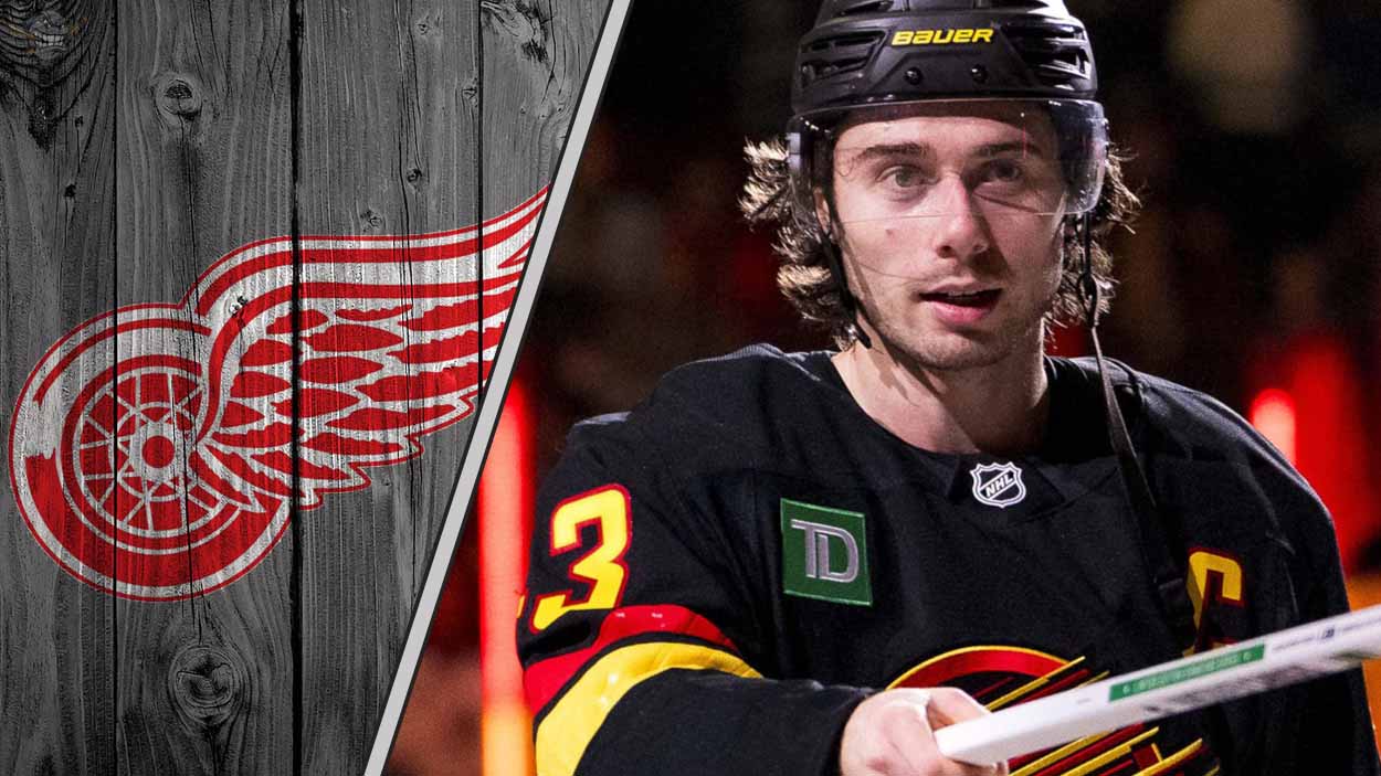 Quinn Hughes skates in his Vancouver Canucks jersey, looking focused during an NHL game, with the Detroit Red Wings logo in the background.