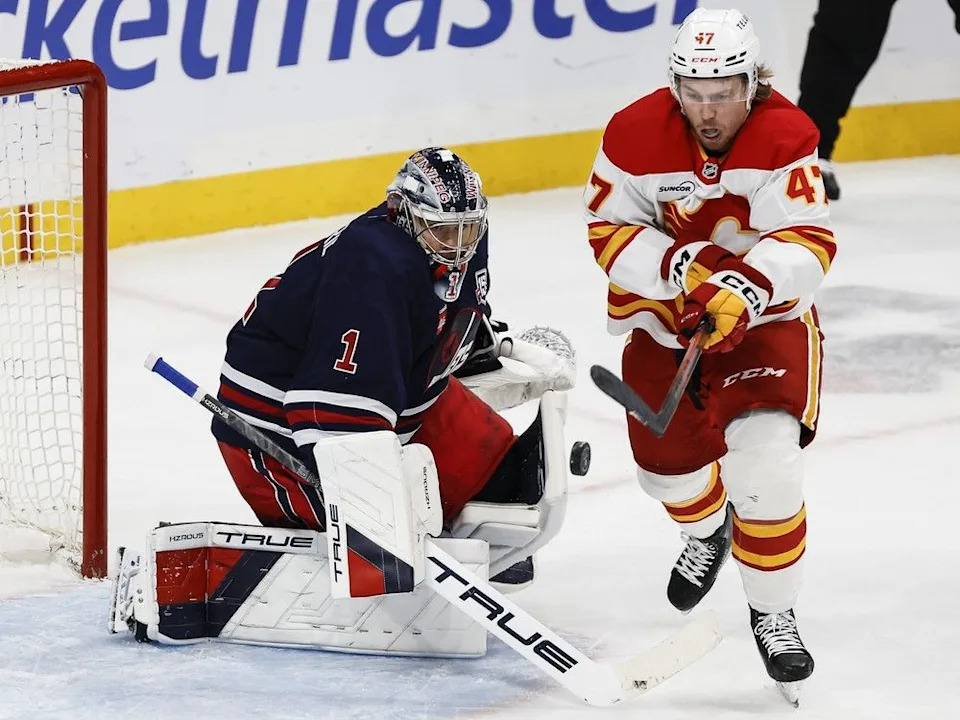 Flames forward Connor Zary knocks down his own rebound off Jets goaltender Eric Comrie on Friday.