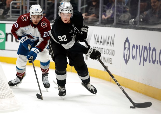 The Kings’ Brandt Clarke, right, skates with the puck as...