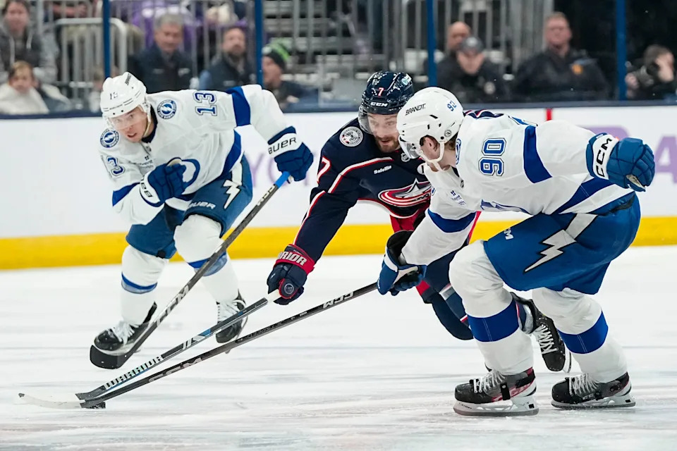 Blue Jackets center Sean Kuraly (7) skates between Lightning right wing Cam Atkinson (13) and defenseman J.J. Moser (90) during a game on Nov. 21, 2024. The Blue Jackets won 7-6 in overtime.