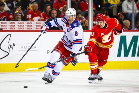 J.T. Miller of the New York Rangers (#8) trying to shield the puck from Calgary Flames captain Mikael Backlund (#11).
